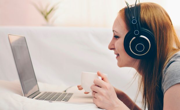 Lady on computer with headphones and tea during social isolation