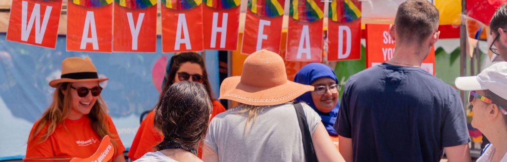 WayAhead staff at Fair Day stand interacting with visitors. There is "WayAhead" written in bright orange lettering across the top of the stand.