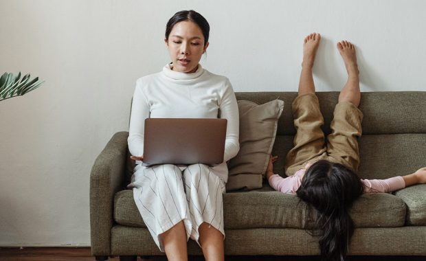 Woman working from home on the couch with a playful child beside her